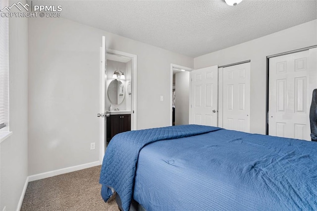 bedroom featuring ensuite bath, baseboards, carpet floors, and a textured ceiling