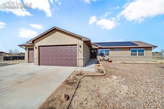 ranch-style house with a garage, concrete driveway, roof mounted solar panels, and stucco siding