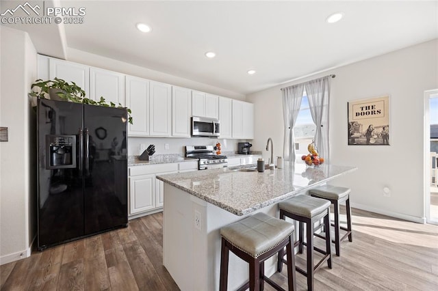 kitchen with wood finished floors, appliances with stainless steel finishes, a sink, and white cabinetry