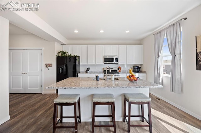 kitchen featuring white cabinets, appliances with stainless steel finishes, a breakfast bar, wood finished floors, and a sink