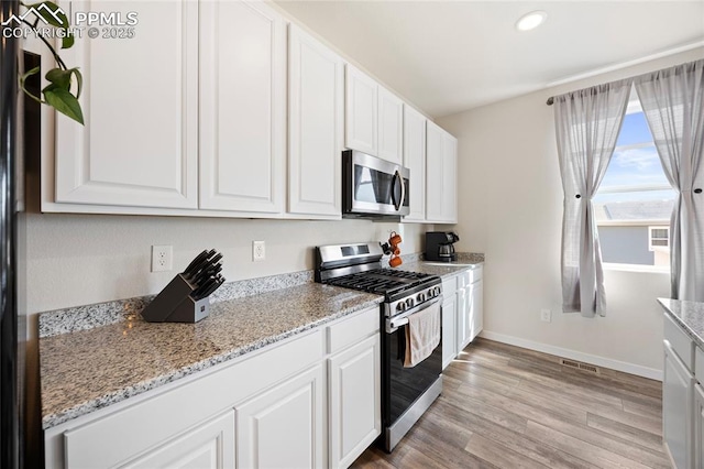 kitchen with appliances with stainless steel finishes, white cabinets, light wood-style floors, and baseboards