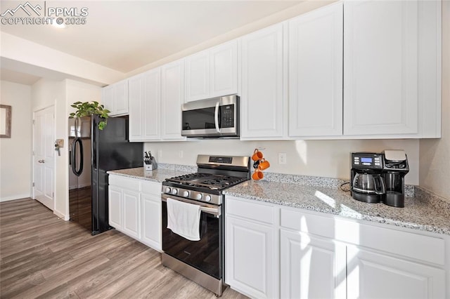 kitchen featuring appliances with stainless steel finishes, white cabinets, light wood-style floors, and light stone countertops