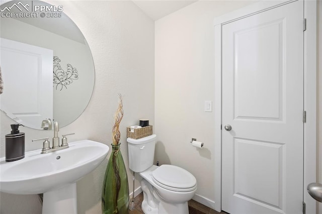 half bath with toilet, baseboards, and a sink