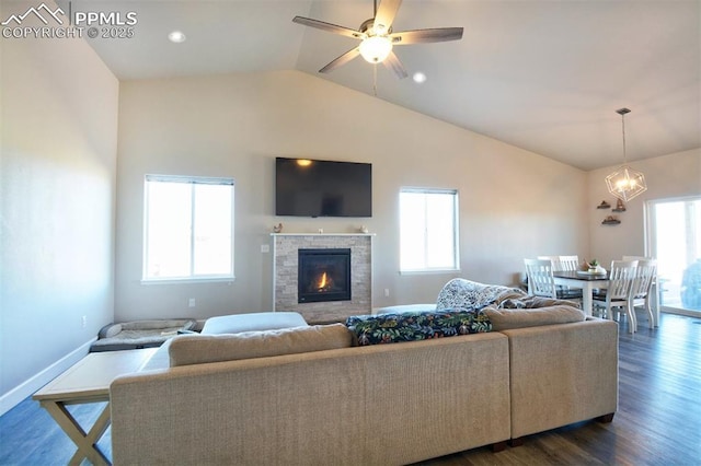 living area featuring a fireplace, dark wood finished floors, vaulted ceiling, baseboards, and ceiling fan with notable chandelier