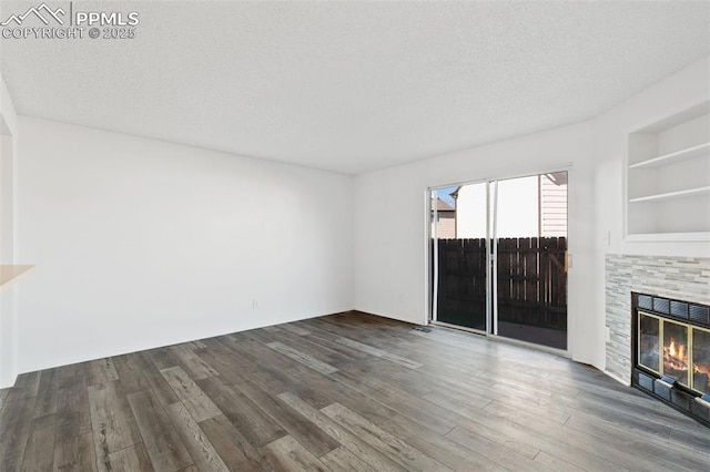 unfurnished living room with dark wood-style floors, built in features, a textured ceiling, and a glass covered fireplace