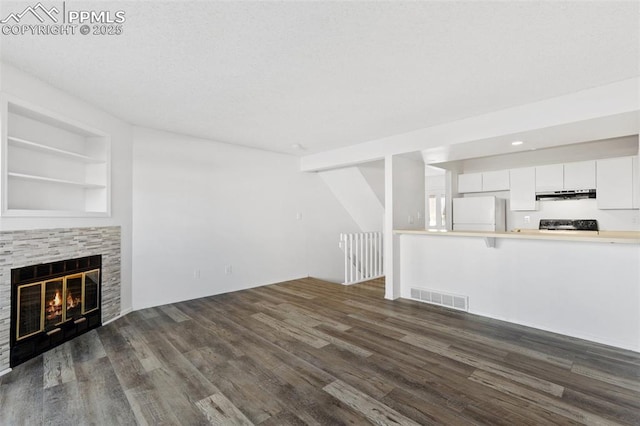 unfurnished living room featuring dark wood-style flooring, visible vents, and a fireplace