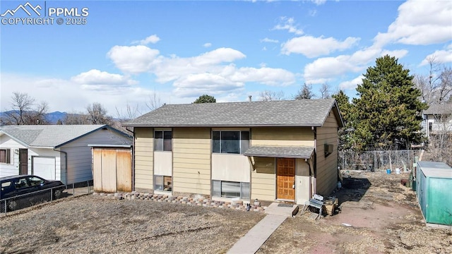 view of front of house featuring roof with shingles, fence, and an outdoor structure