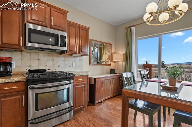 kitchen with decorative backsplash, light wood-style flooring, appliances with stainless steel finishes, brown cabinets, and an inviting chandelier