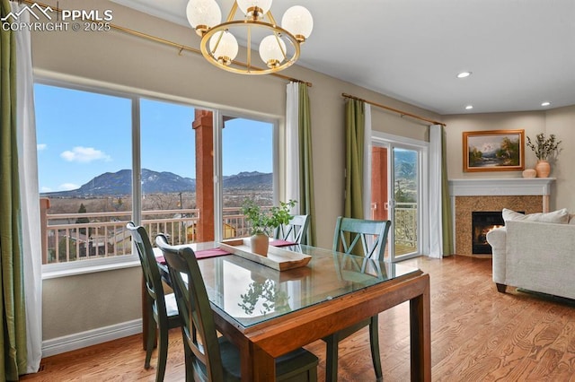 dining room with a chandelier, a mountain view, baseboards, a lit fireplace, and light wood finished floors