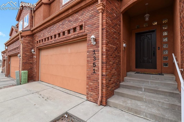 property entrance with a garage, brick siding, and driveway