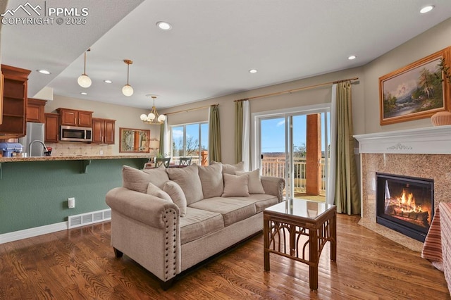 living room with dark wood-style floors, a chandelier, visible vents, and a premium fireplace