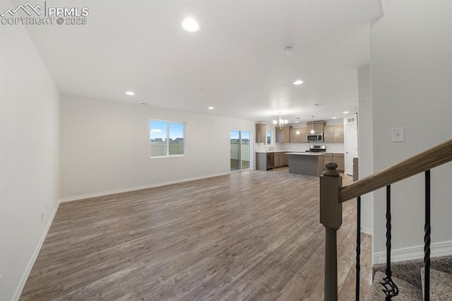 unfurnished living room with recessed lighting, a notable chandelier, baseboards, and wood finished floors