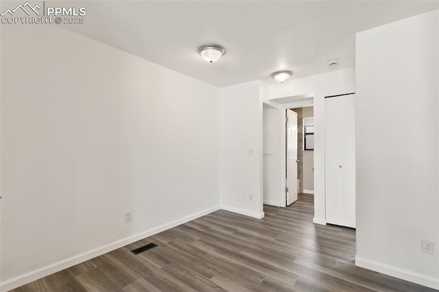 empty room with baseboards, visible vents, and dark wood-type flooring