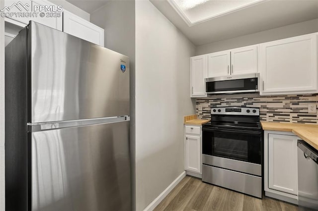 kitchen with appliances with stainless steel finishes, wood counters, white cabinets, and tasteful backsplash