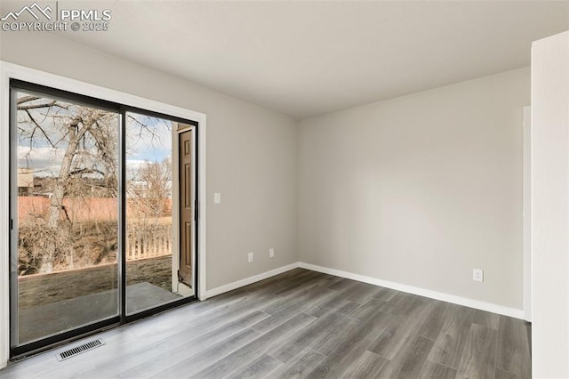 empty room featuring wood finished floors, visible vents, and baseboards