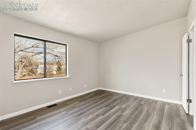 empty room featuring baseboards, visible vents, and wood finished floors