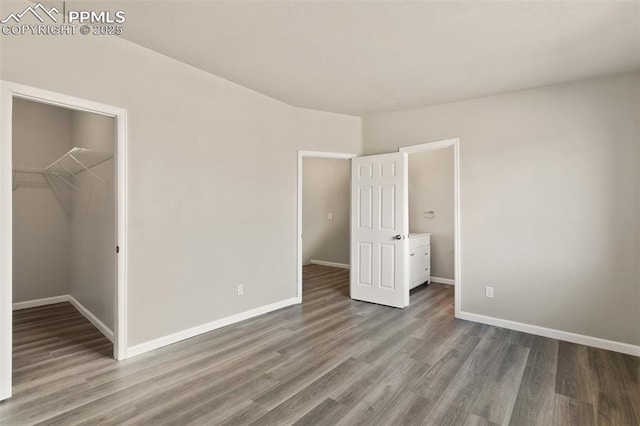 unfurnished bedroom featuring a walk in closet, baseboards, and wood finished floors