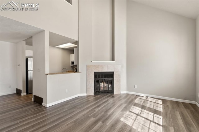 unfurnished living room with dark wood-style flooring, a high ceiling, and a tiled fireplace