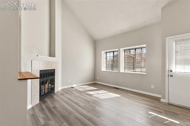 unfurnished living room featuring high vaulted ceiling, baseboards, a tiled fireplace, and wood finished floors