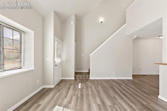 interior space featuring stairs, a high ceiling, baseboards, and wood finished floors