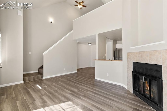 unfurnished living room featuring a fireplace, wood finished floors, a towering ceiling, baseboards, and stairs