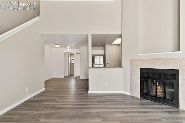 unfurnished living room with wood finished floors, a tile fireplace, and baseboards