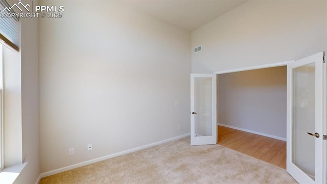 carpeted spare room with french doors, a towering ceiling, visible vents, and baseboards