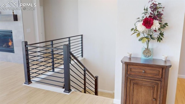 staircase featuring baseboards, wood finished floors, and a glass covered fireplace