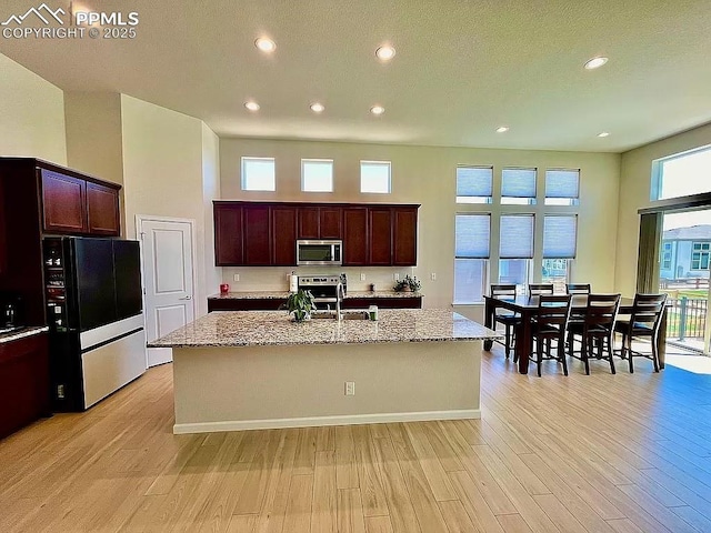 kitchen with stainless steel appliances, light wood-type flooring, a center island with sink, and light stone counters