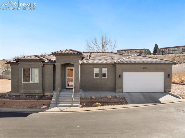 mediterranean / spanish house with an attached garage, a tiled roof, concrete driveway, and stucco siding