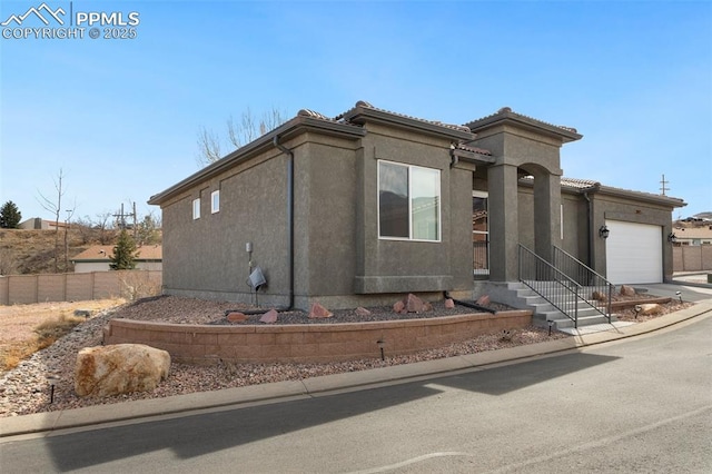 view of side of home featuring an attached garage, a tile roof, fence, concrete driveway, and stucco siding