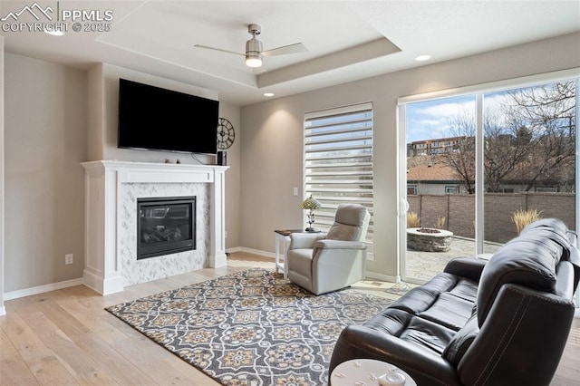 living area featuring baseboards, a ceiling fan, a premium fireplace, wood finished floors, and a tray ceiling