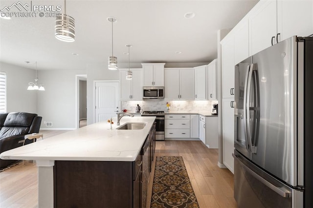 kitchen featuring appliances with stainless steel finishes, backsplash, light wood-type flooring, white cabinetry, and a sink