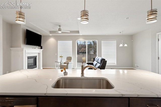 kitchen featuring a center island with sink, a raised ceiling, open floor plan, a fireplace, and a sink