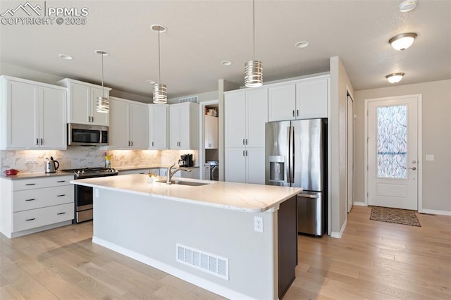 kitchen with tasteful backsplash, visible vents, appliances with stainless steel finishes, a kitchen island with sink, and a sink