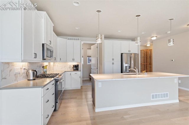 kitchen featuring visible vents, backsplash, stainless steel appliances, light wood-style floors, and a sink