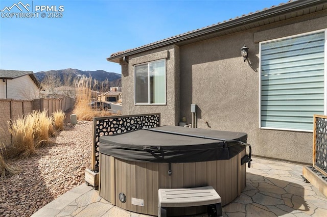 view of patio with a mountain view, a hot tub, and fence