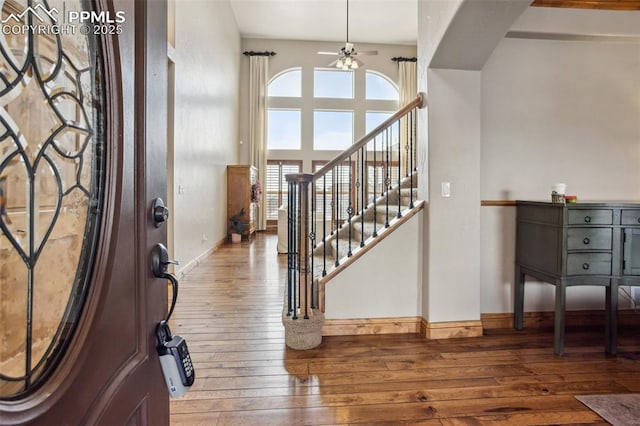 foyer entrance with baseboards, a towering ceiling, ceiling fan, stairway, and hardwood / wood-style floors