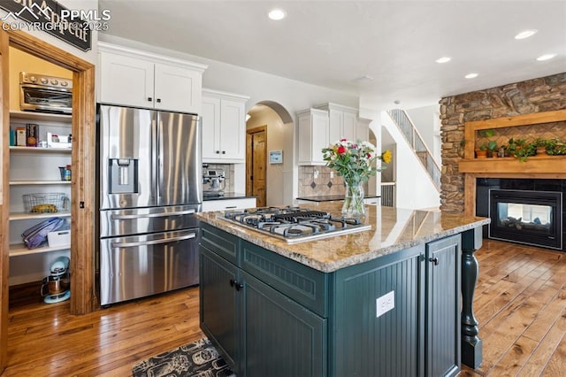 kitchen featuring white cabinets, decorative backsplash, light wood-style flooring, stainless steel appliances, and a fireplace