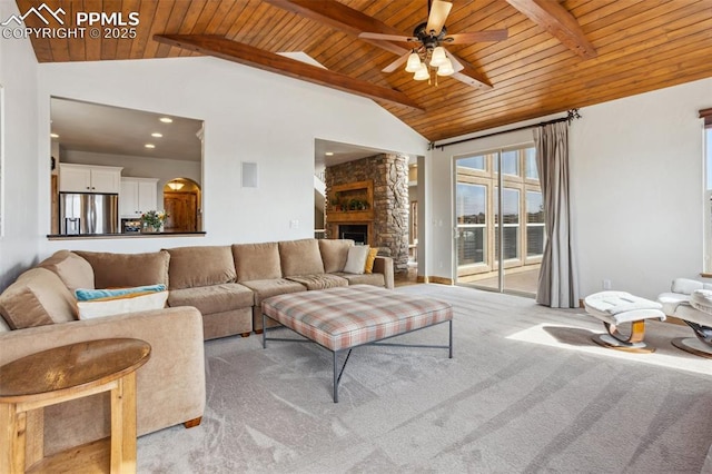 living room with beam ceiling, light colored carpet, ceiling fan, a stone fireplace, and wooden ceiling