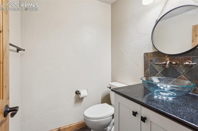 half bathroom featuring toilet, a textured wall, and vanity