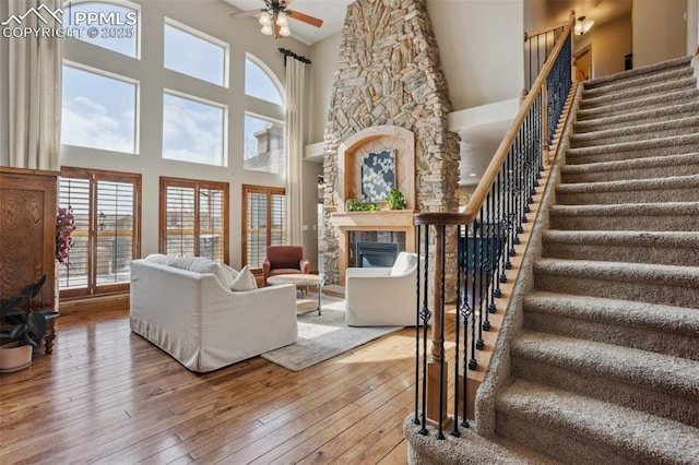 living room with stairs, a stone fireplace, hardwood / wood-style flooring, and a ceiling fan