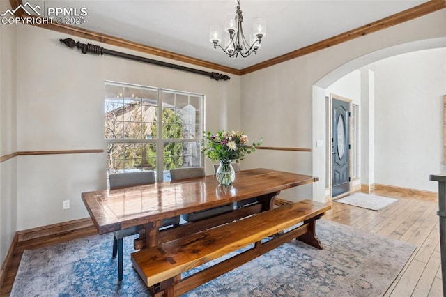 dining room featuring arched walkways, baseboards, wood finished floors, crown molding, and a notable chandelier