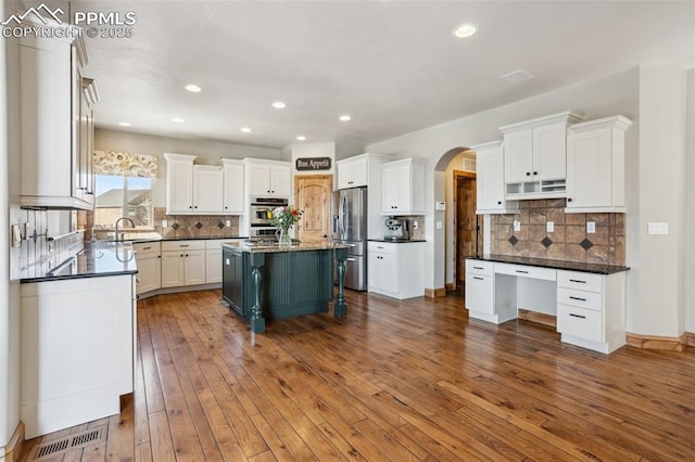 kitchen featuring arched walkways, dark wood-style flooring, dark countertops, white cabinetry, and stainless steel fridge with ice dispenser