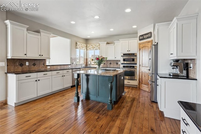 kitchen with white cabinetry, a kitchen island, appliances with stainless steel finishes, and hardwood / wood-style floors