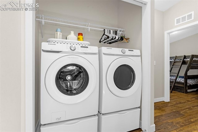 clothes washing area with laundry area, wood finished floors, visible vents, and washing machine and clothes dryer