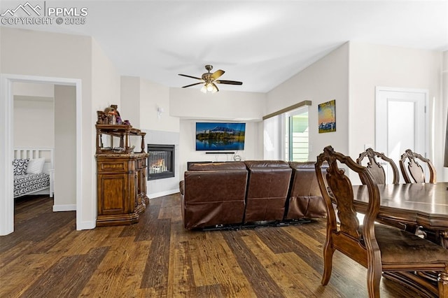 living area with dark wood finished floors, a glass covered fireplace, baseboards, and ceiling fan