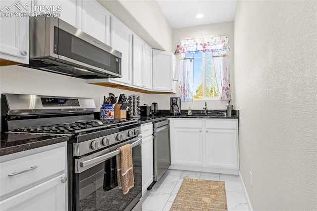 kitchen featuring dark stone countertops, a sink, stainless steel appliances, white cabinetry, and marble finish floor