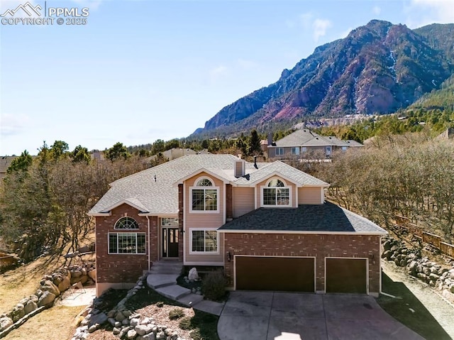 traditional-style house featuring an attached garage, a mountain view, brick siding, a shingled roof, and driveway