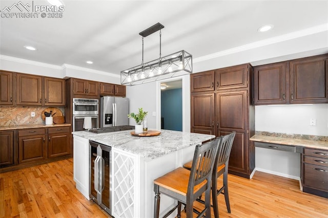 kitchen featuring beverage cooler, stainless steel appliances, light wood-style floors, built in study area, and crown molding